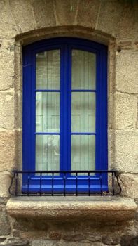 Charming blue window with iron railing on rustic stone wall showcasing classic architecture.