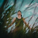 一名年轻人闭着眼睛，在户外的草丛中放松冥想，拥抱大自然