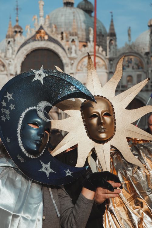 Free Colorful Venetian masks depicting sun and moon against St Mark's Basilica backdrop. Stock Photo