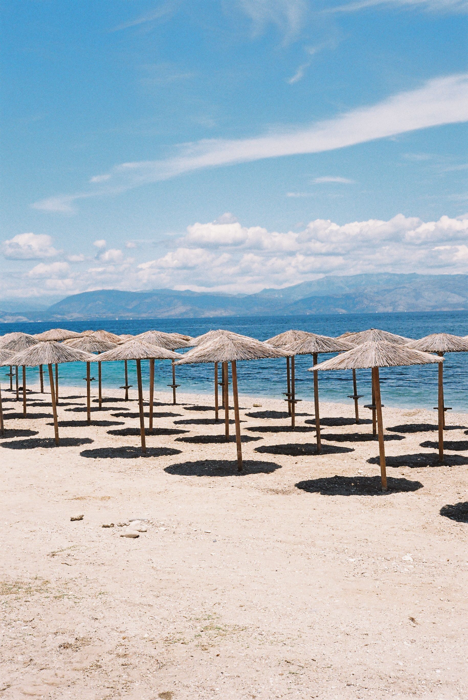 A serene beach scene with rows of straw umbrellas by the ocean under a clear blue sky.