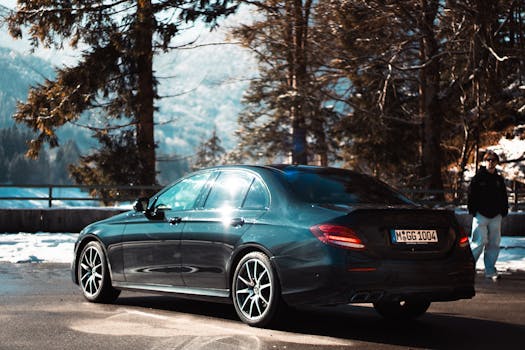 Luxury black sedan parked on scenic winter mountain road with clear blue sky.