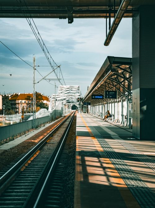 Free Empty train platform with tracks leading to a distant bridge on a sunny day. Stock Photo