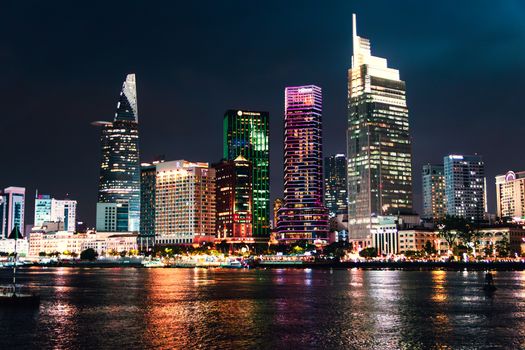 Stunning night view of Ho Chi Minh City skyline with colorful illuminated skyscrapers reflecting on the river.