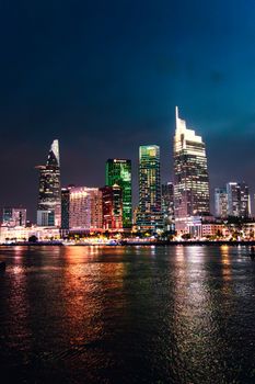 Vibrant night view of Hồ Chí Minh City skyline reflecting on the river, showcasing modern architecture.
