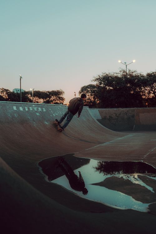 Free Male skateboarder rides ramp at a skate park during twilight with reflections in a puddle. Stock Photo