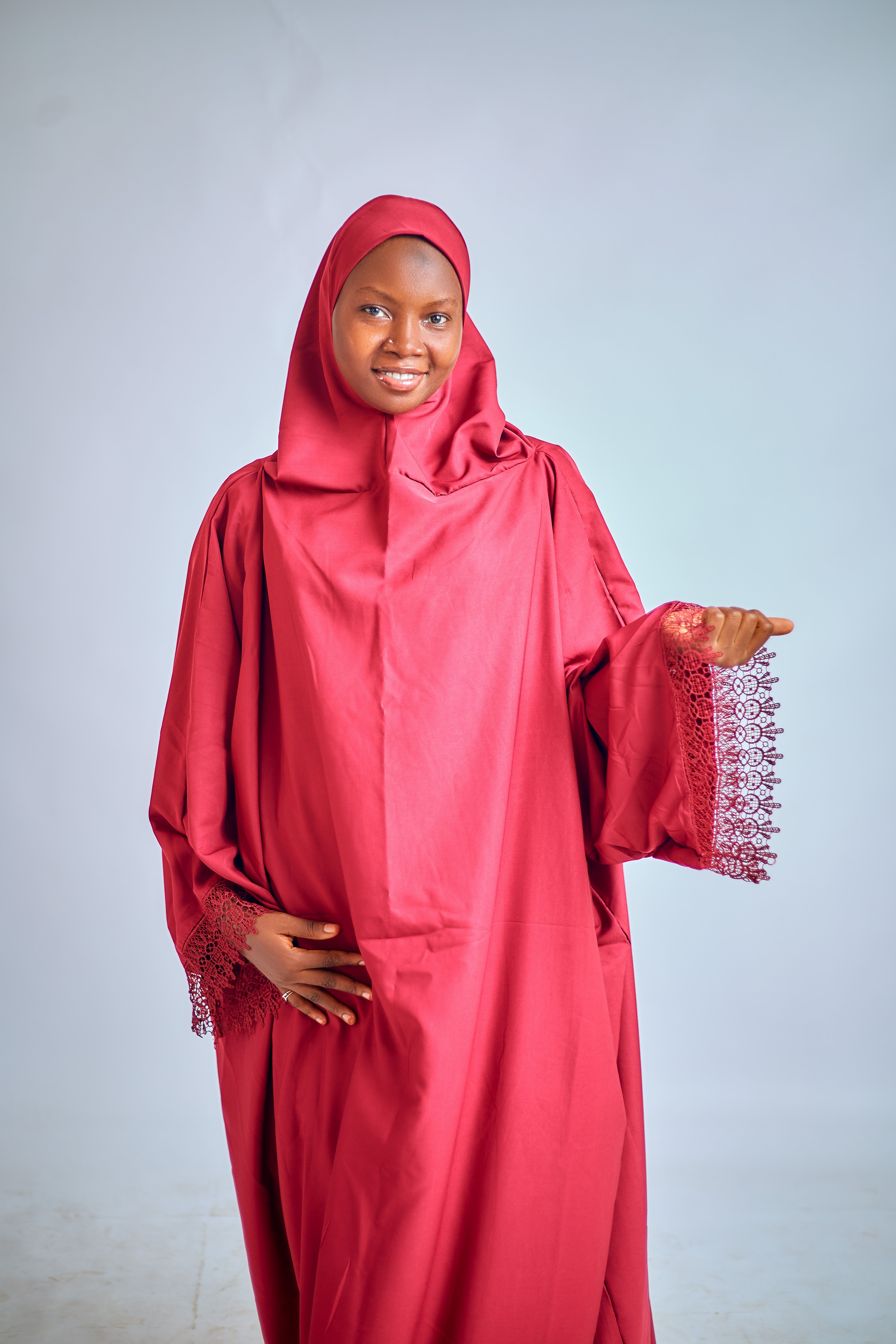 A woman in a red hijab, smiling and posing confidently against a neutral background.