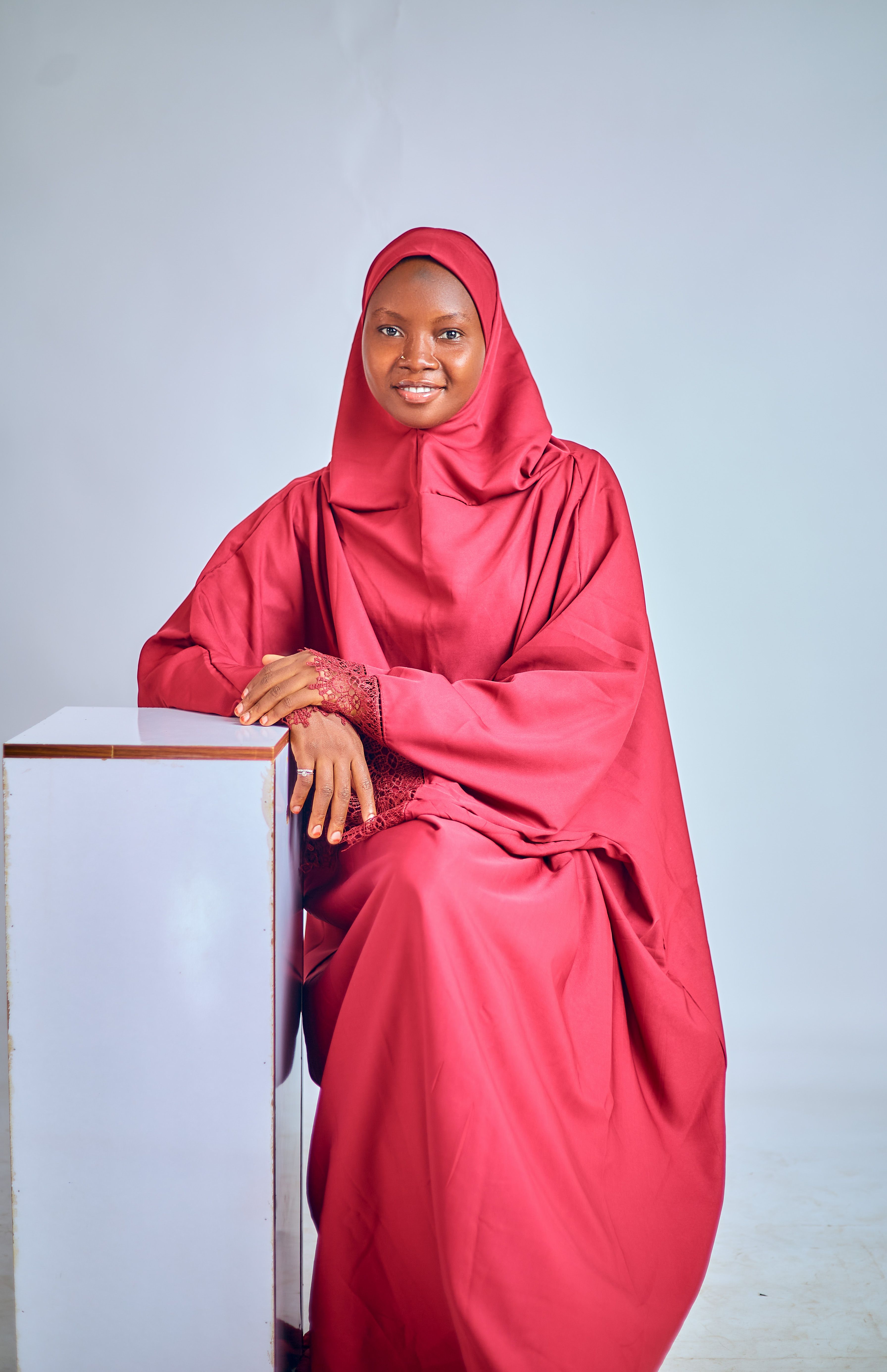 Portrait of a woman dressed elegantly in a red hijab against a neutral backdrop.