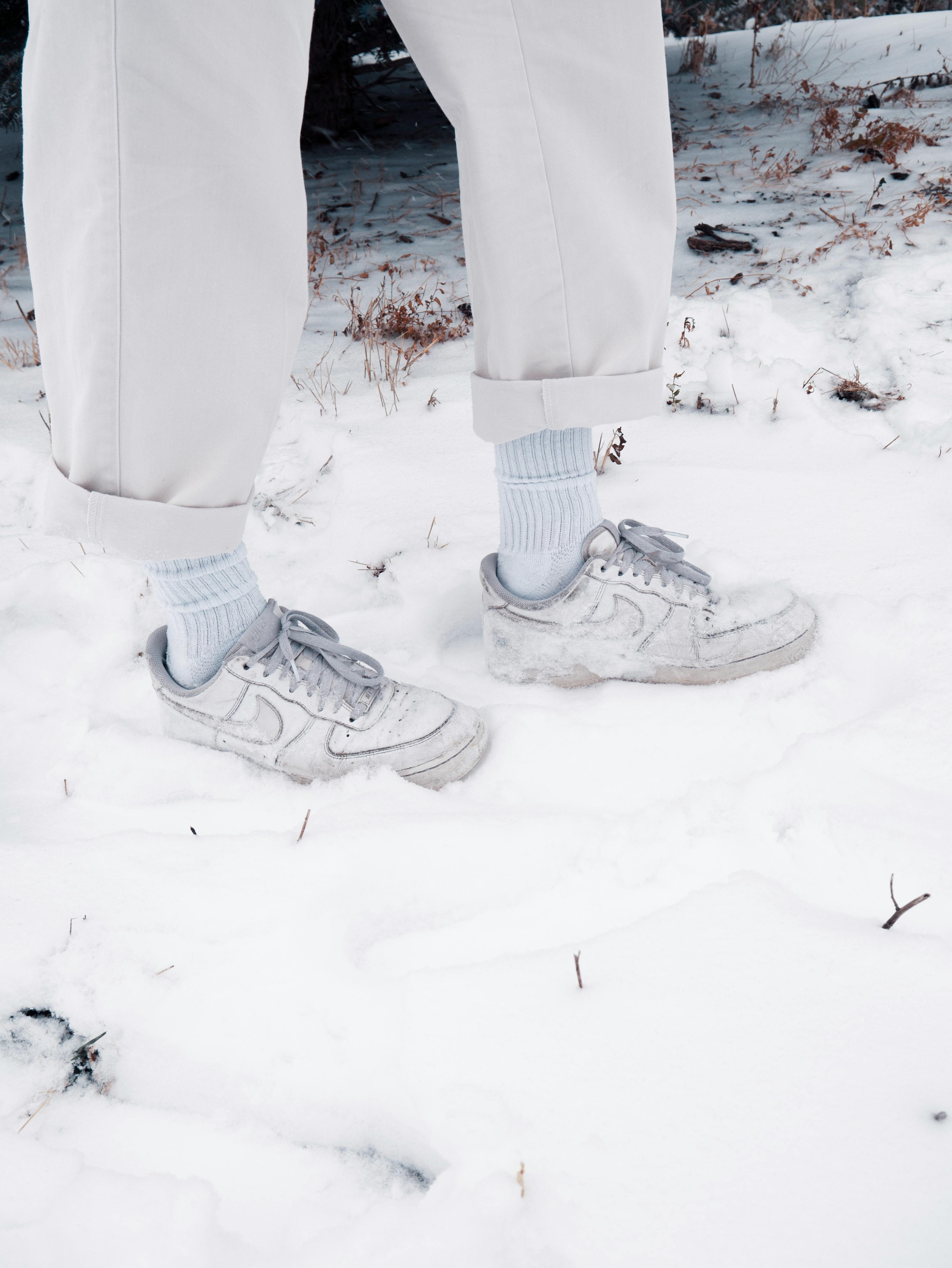 person in white pants and nike shoes standing on snowy ground