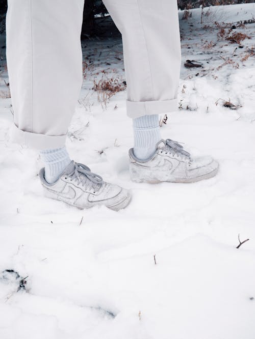 Person in White Pants and Nike Shoes Standing on Snowy Ground