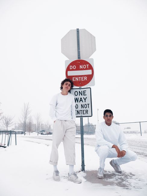 Two men in white outfits posed by street signs in a snowy urban setting.