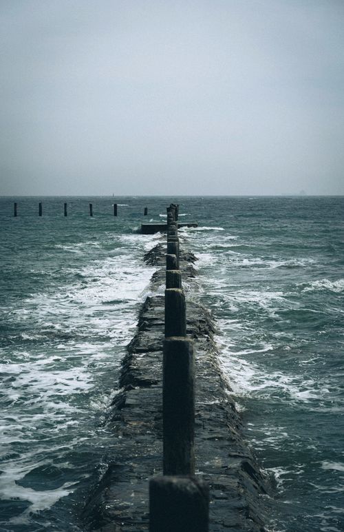 Free Dramatic view of a seawall stretching into the endless ocean under cloudy skies. Stock Photo