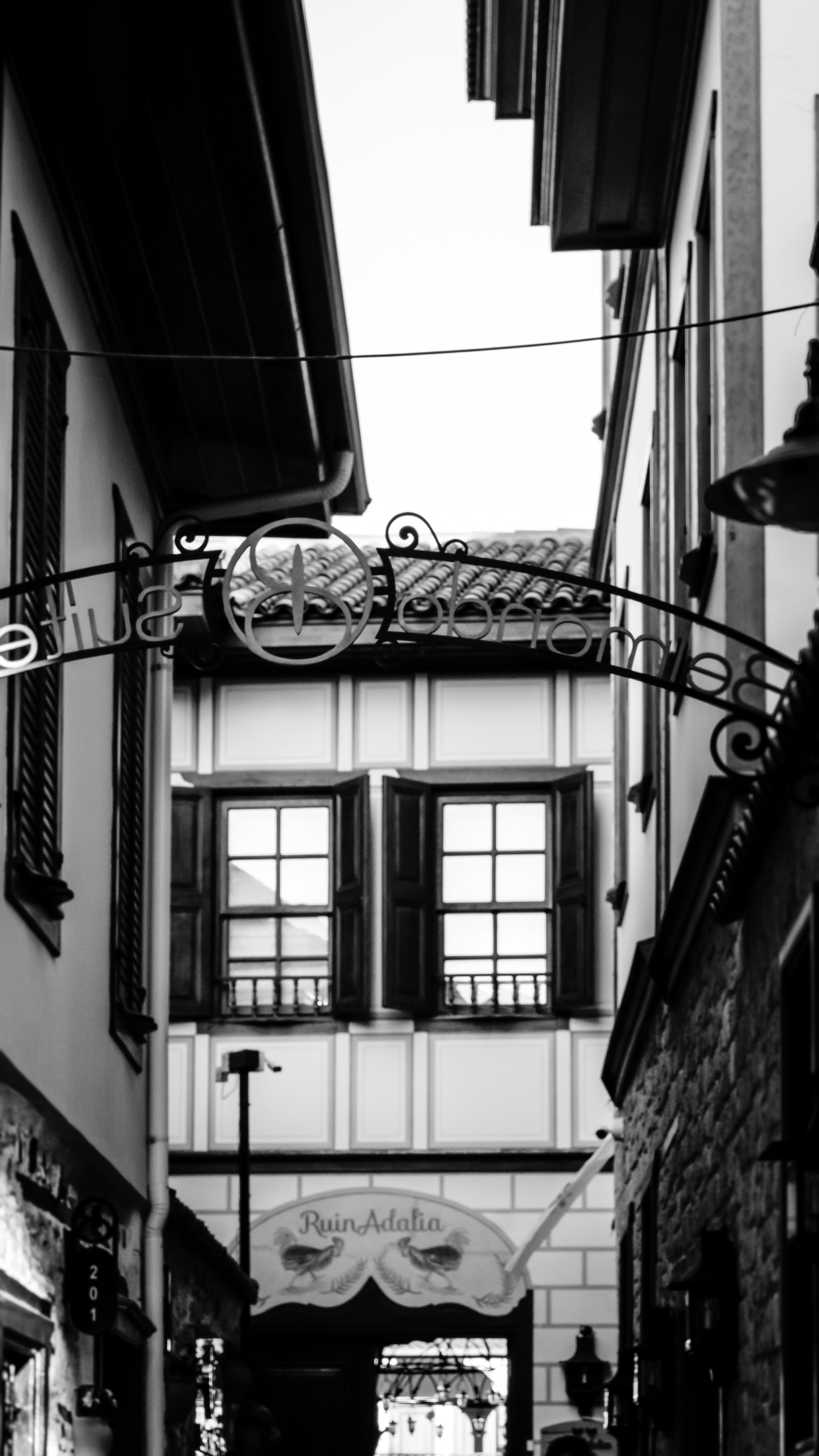 Charming black and white photo of a narrow alleyway with vintage architectural elements and decorative sign.