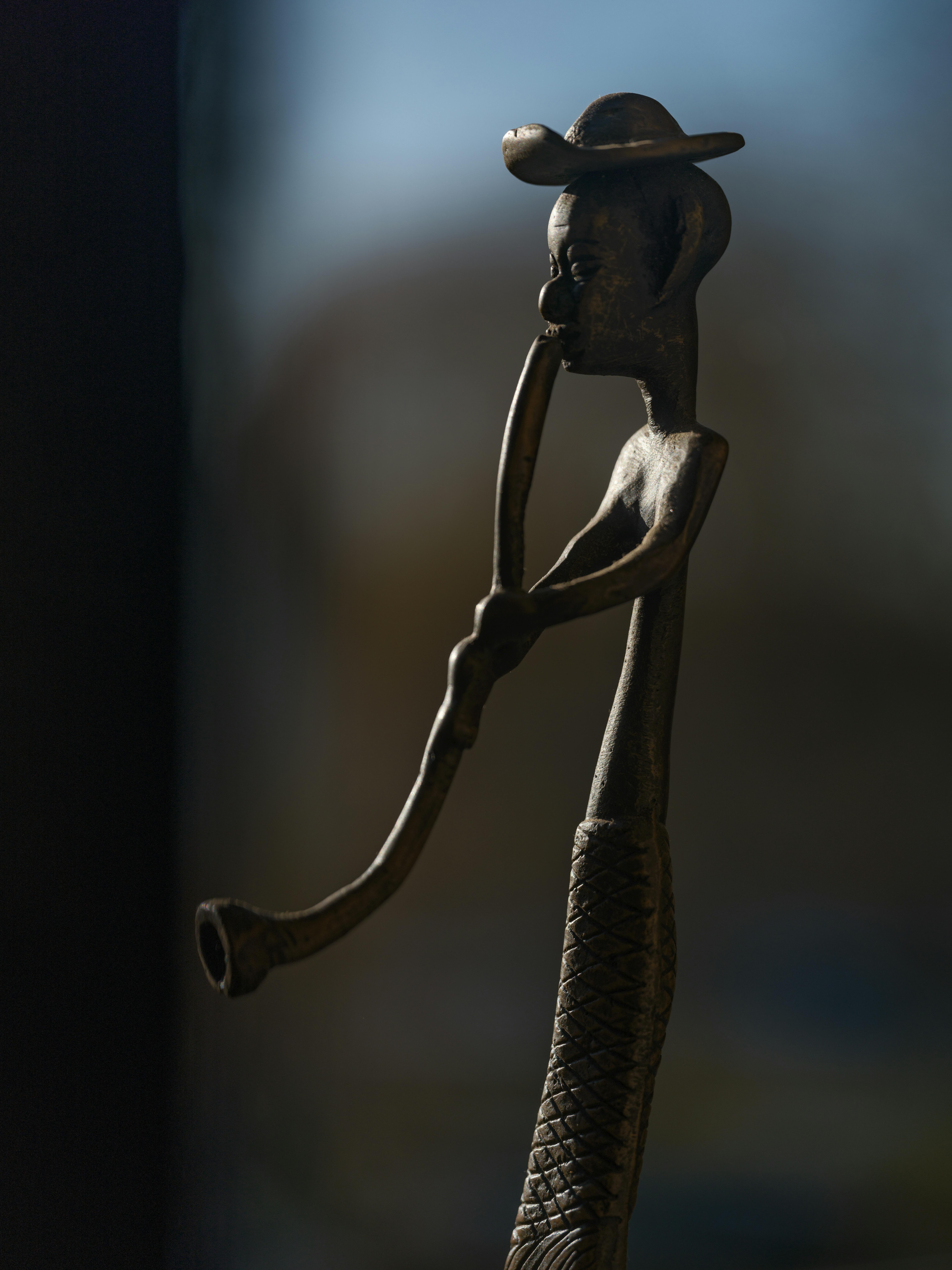 Free Artistic bronze sculpture of an African figure playing a trumpet, beautifully silhouetted against a window. Stock Photo