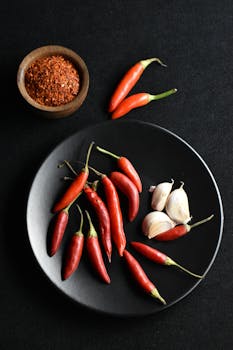 Aesthetic composition of red chili peppers, garlic, and chili flakes on black background.