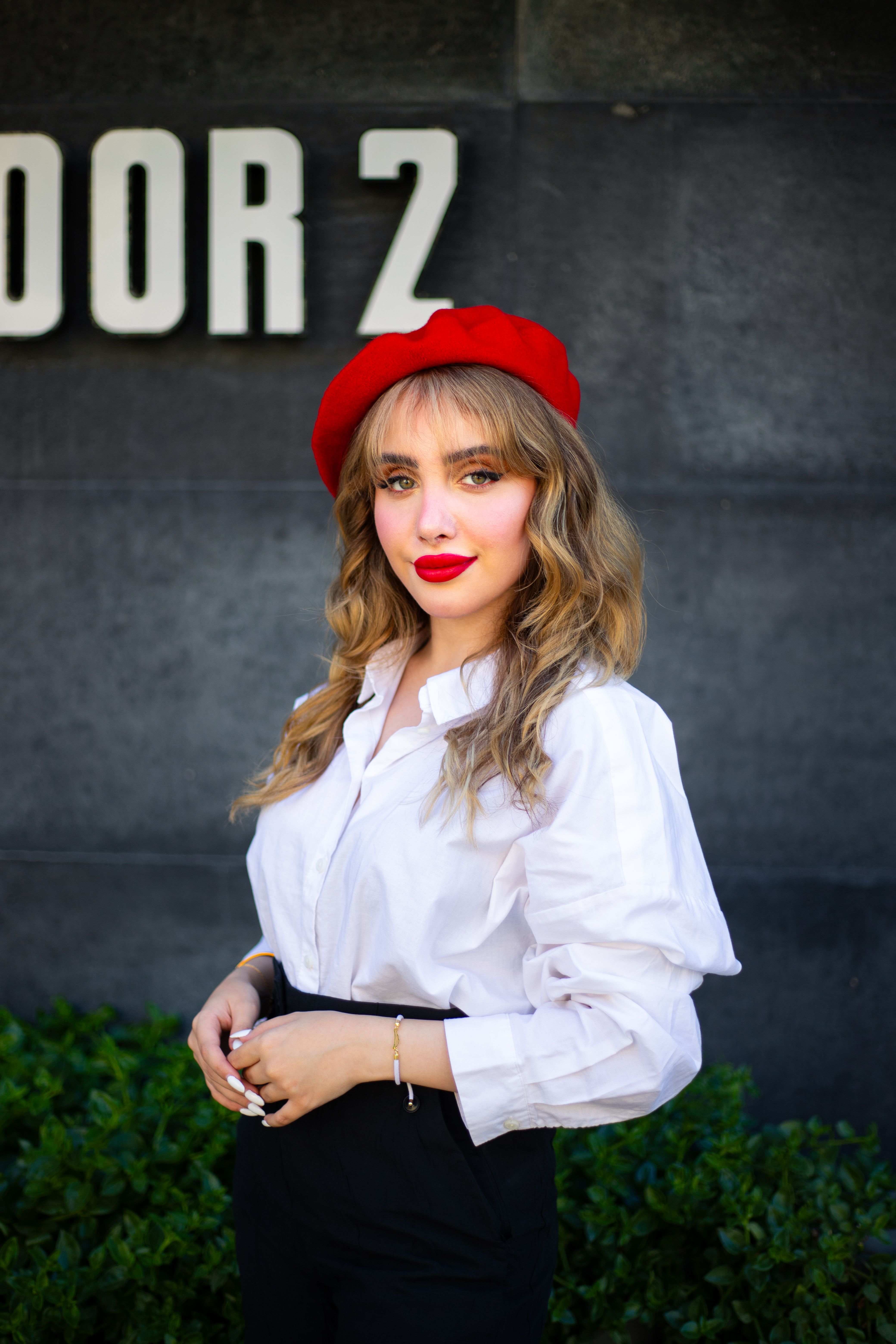 Fashionable woman in a red beret posing gracefully beside a sign with 'Door 2'.