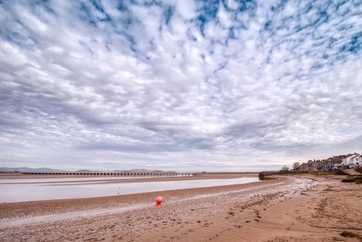 Cloudy sky over Arnside beach in Cumbria, UK, with a picturesque promenade and viaduct.