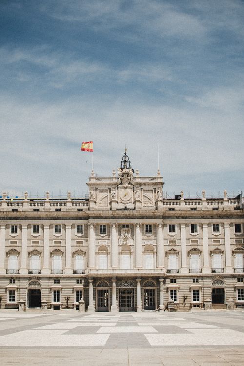 Free Front view of the Royal Palace of Madrid with the Spanish flag against a blue sky. Stock Photo