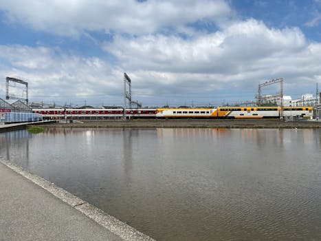 Colorful trains pass by a tranquil waterway under a bright sky in this urban scene near Osaka, Japan.