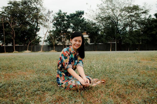 阳光明媚，一位身穿彩色花卉连衣裙的年轻女子微笑着坐在草地上