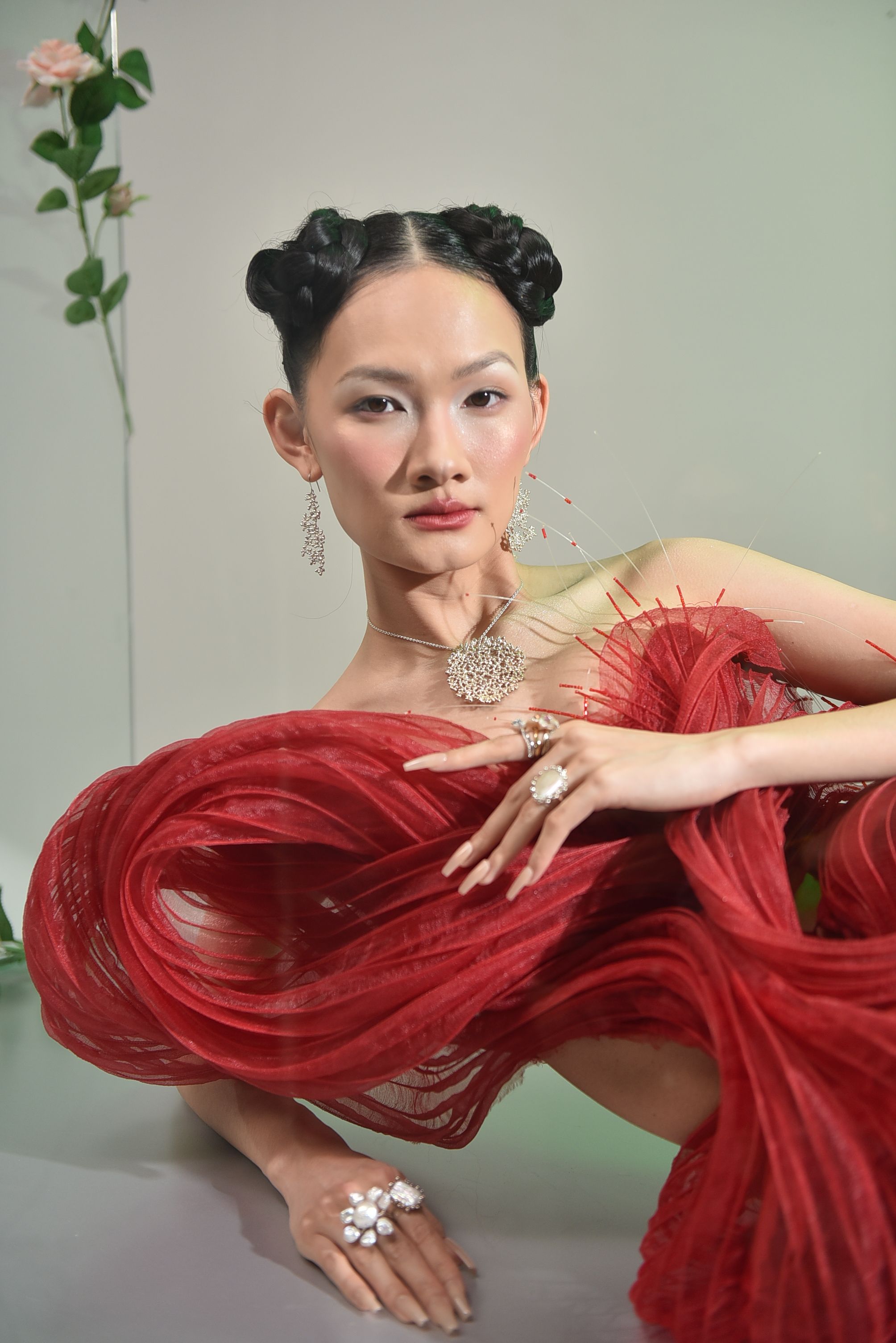 Stylish portrait of a woman in a red gown with artistic design, featuring intricate jewelry and a modern hairstyle.