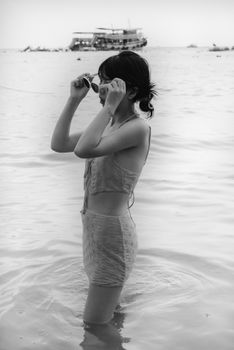 Black and white photo of a woman in swimwear adjusting sunglasses in shallow water.
