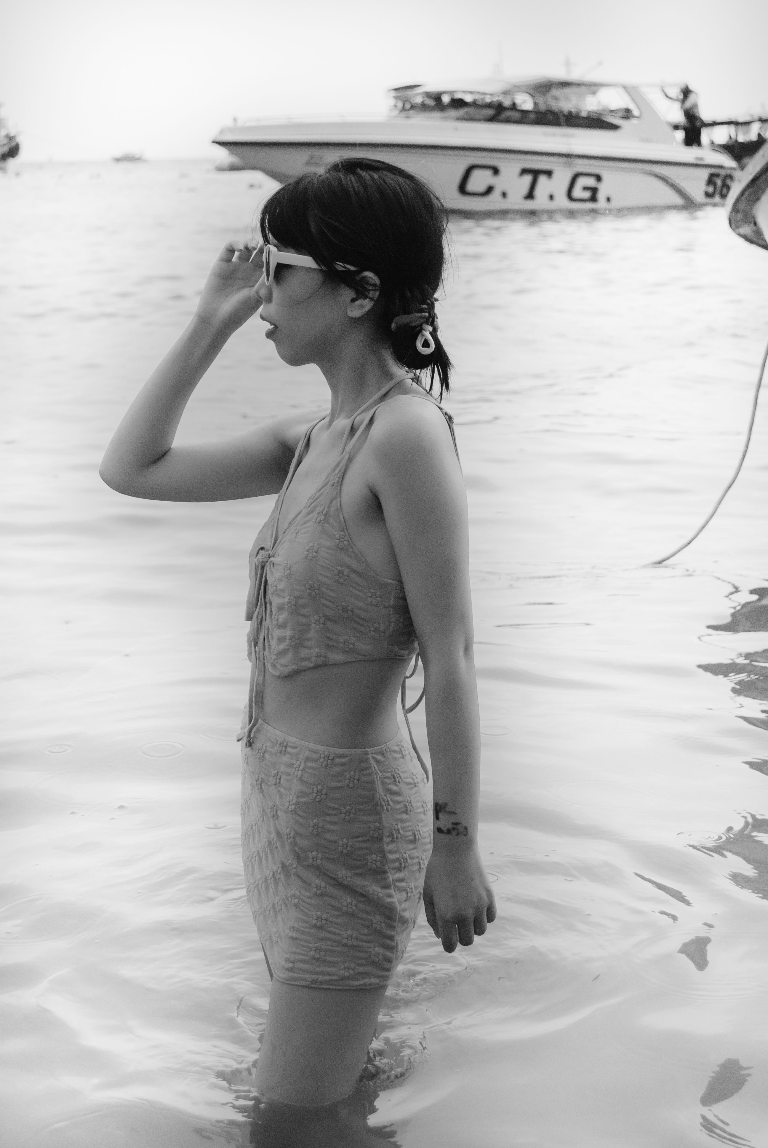 Profile of a woman in swimwear standing in the water by a boat, captured in black and white.