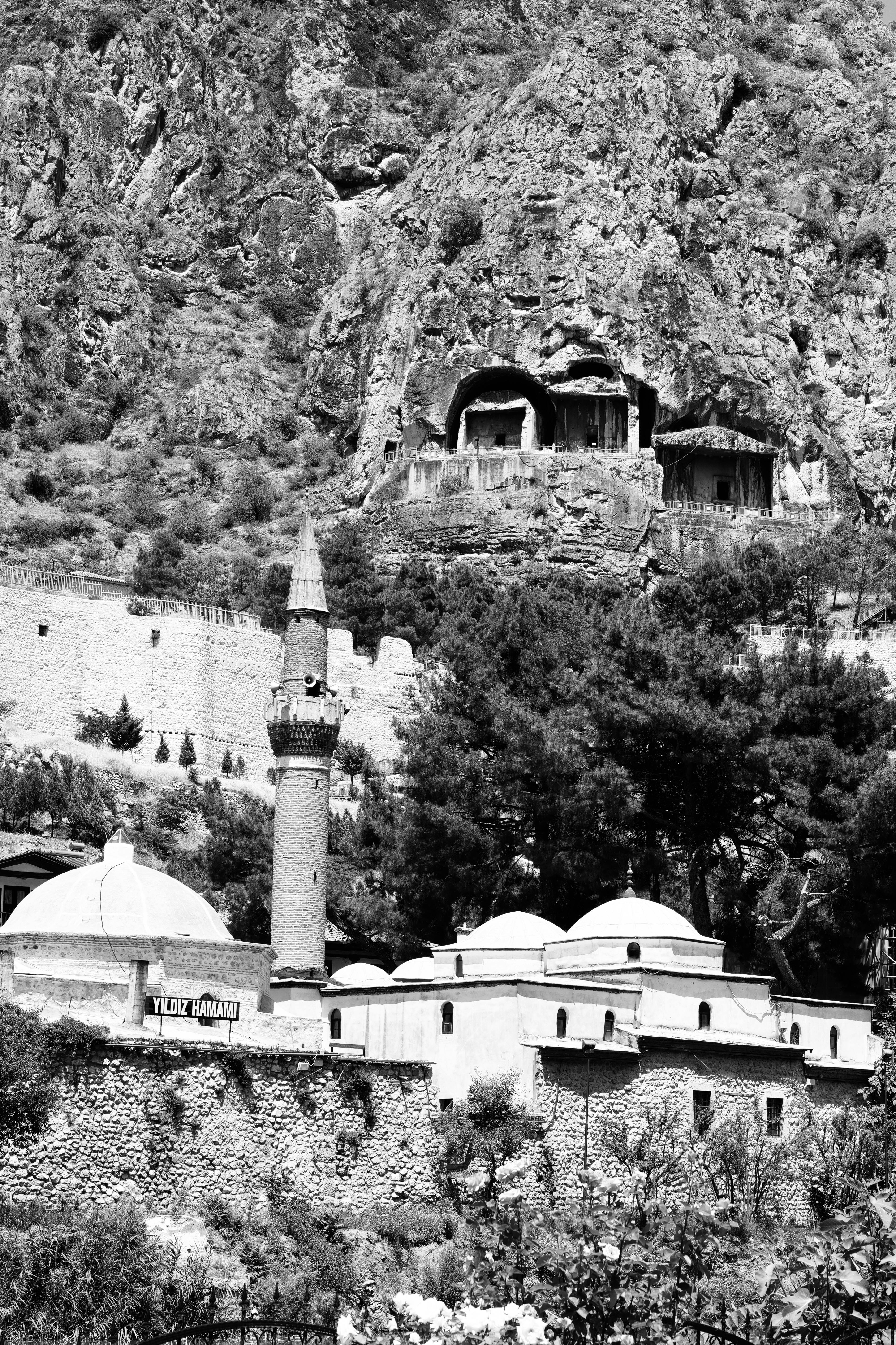 Black and white image of ancient rock tombs and mosque minaret in Amasya, Turkey.