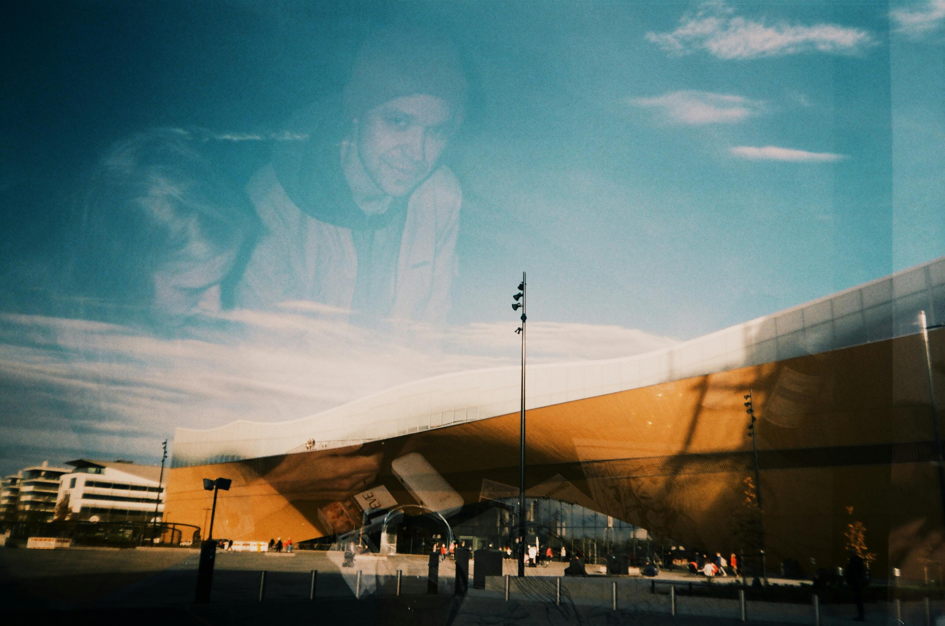 Artistic double exposure of people overlaying modern architectural building exterior in daylight.