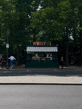 Green street food stand with 'Wurst' sign in a park setting.