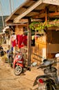 一辆红色摩托车停在雅加达一条阳光明媚的街道上，旁边是传统的木制房屋，屋外挂着晾晒的衣物