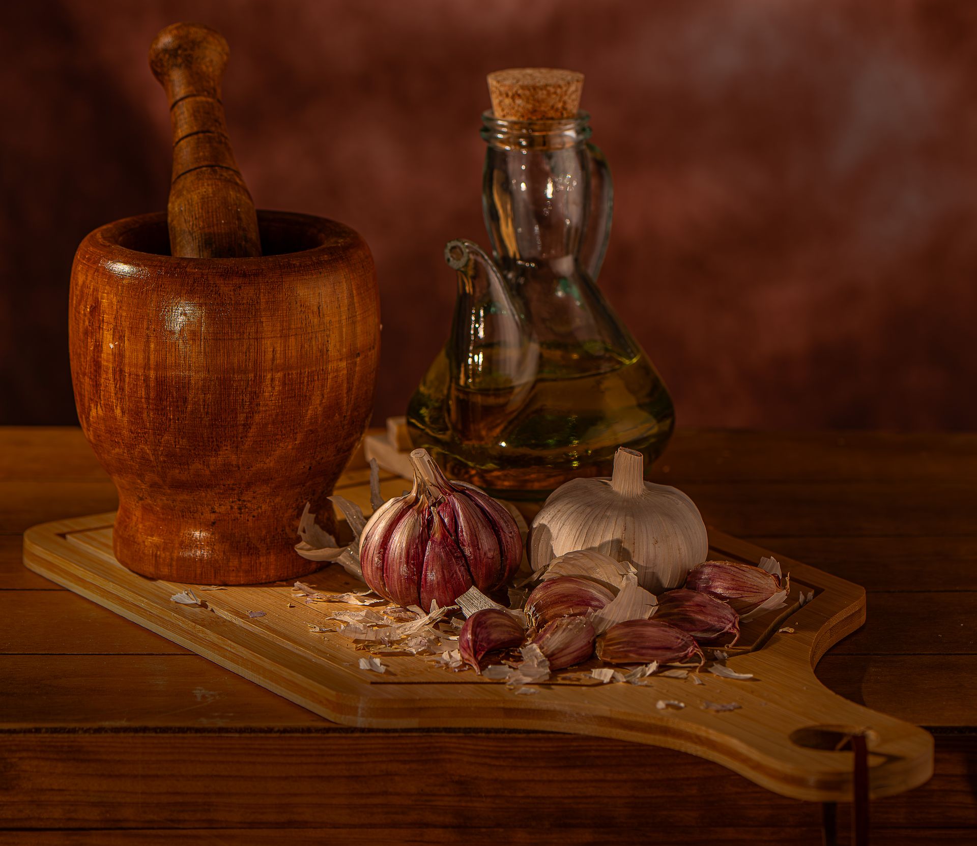 Still life of garlic and olive oil with wooden mortar on cutting board.