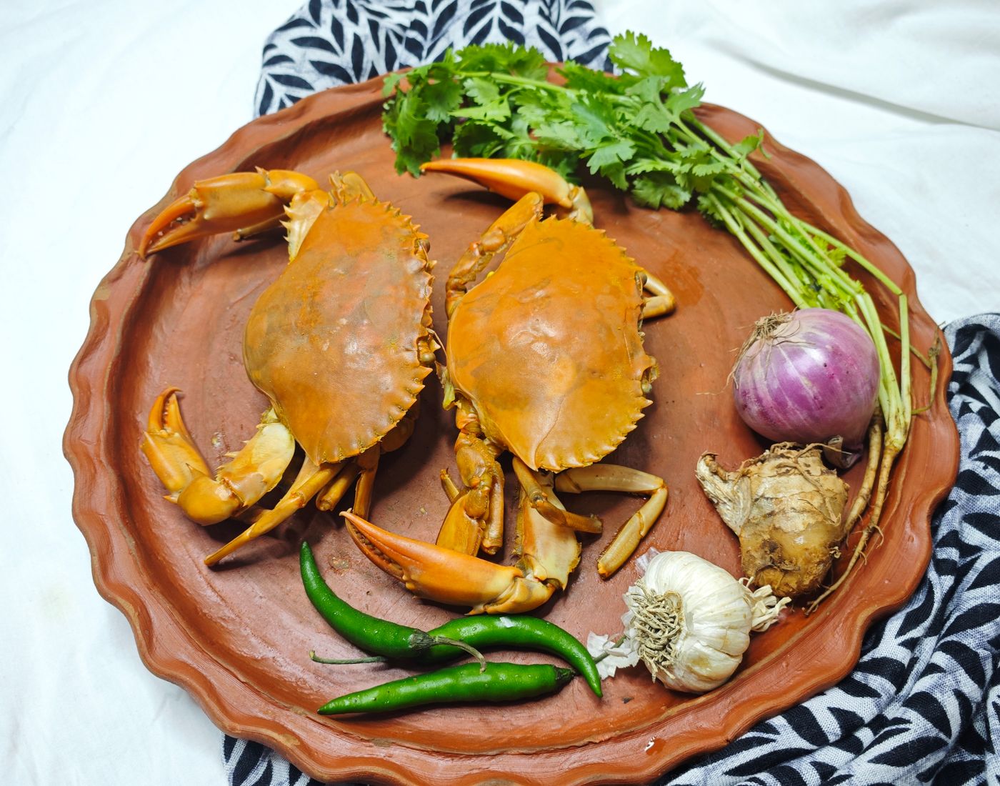 Two fresh crabs with herbs and spices on a rustic tray, ready for cooking.