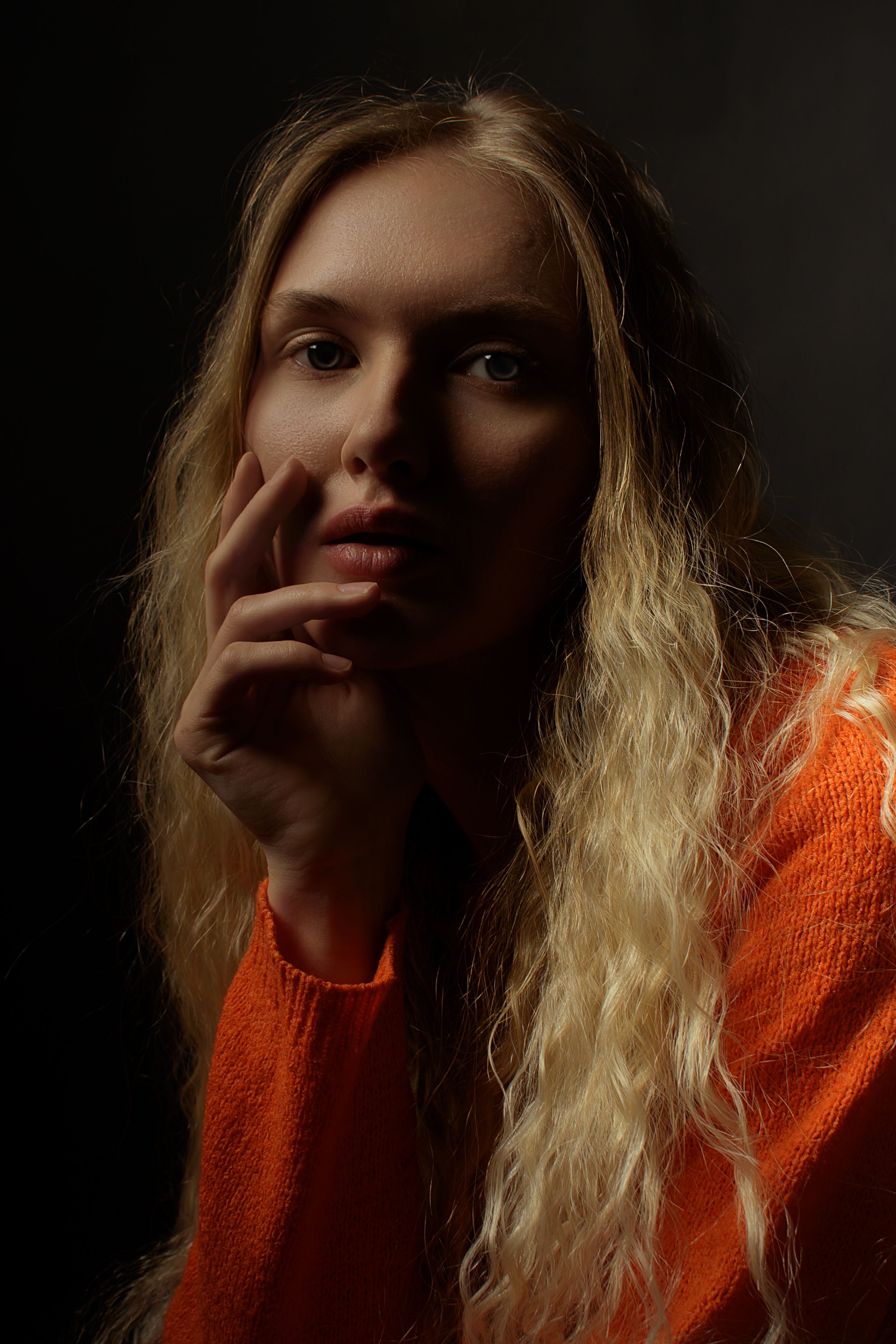 Thoughtful portrait of a woman with long hair in an orange sweater, emphasizing shadows.