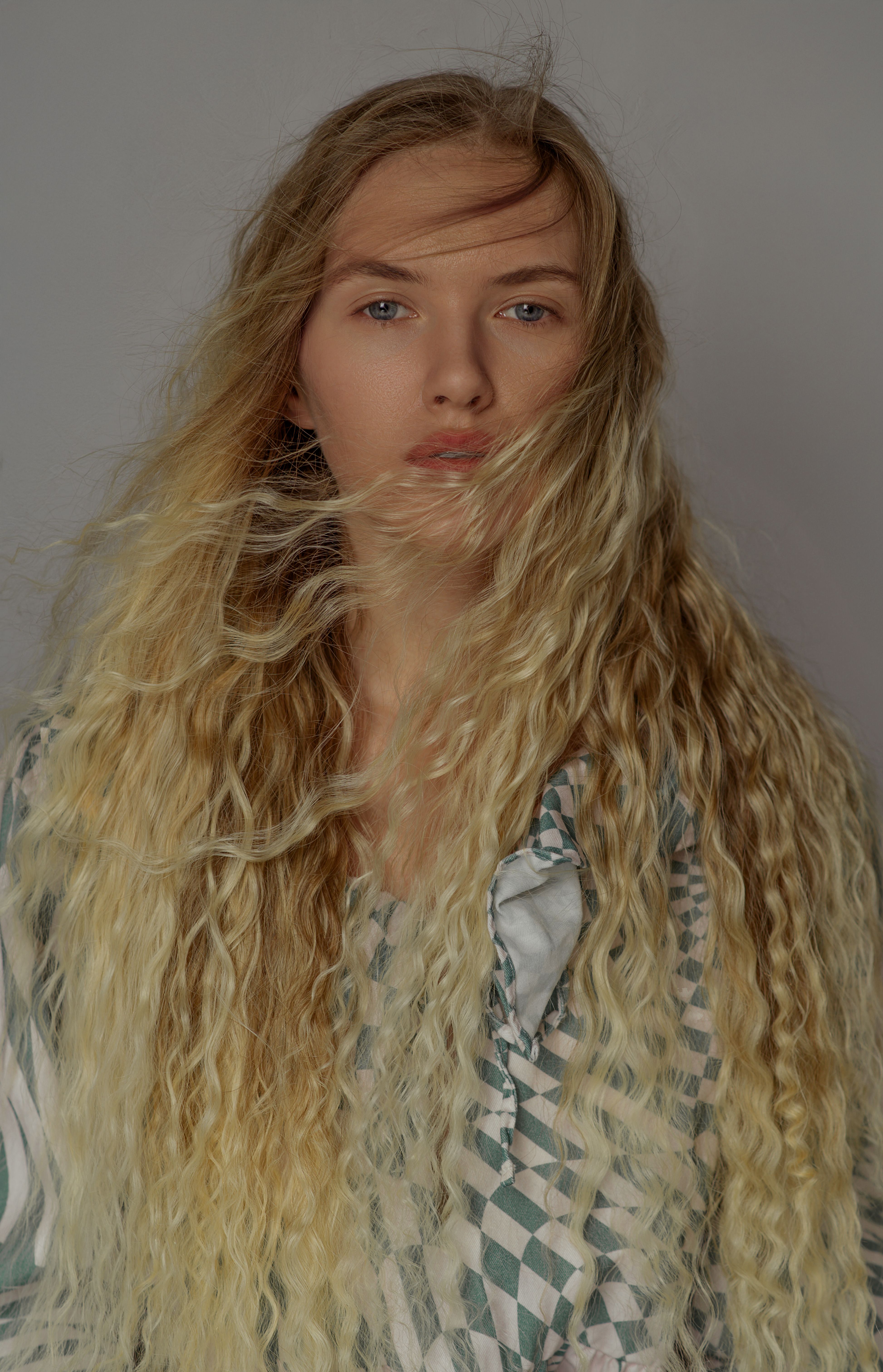 Elegant portrait of a young woman with long wavy blonde hair and a patterned blouse.