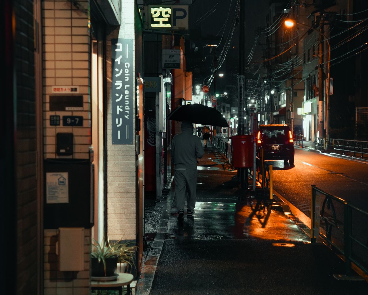a person walks under an umbrella on a dimly lit city street at night r