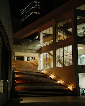 Illuminated modern staircase at night in an urban cityscape, showcasing architectural symmetry.