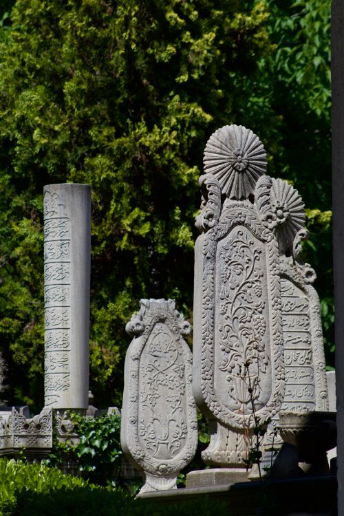 Free Intricately carved tombstones in a lush, peaceful cemetery. Rich cultural heritage displayed in stone designs. Stock Photo