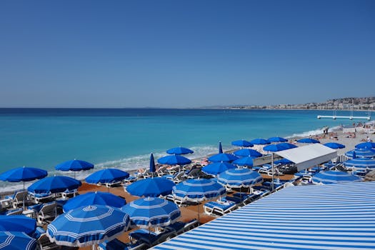 A stunning beach view with blue umbrellas and a clear turquoise sea under a bright sky.