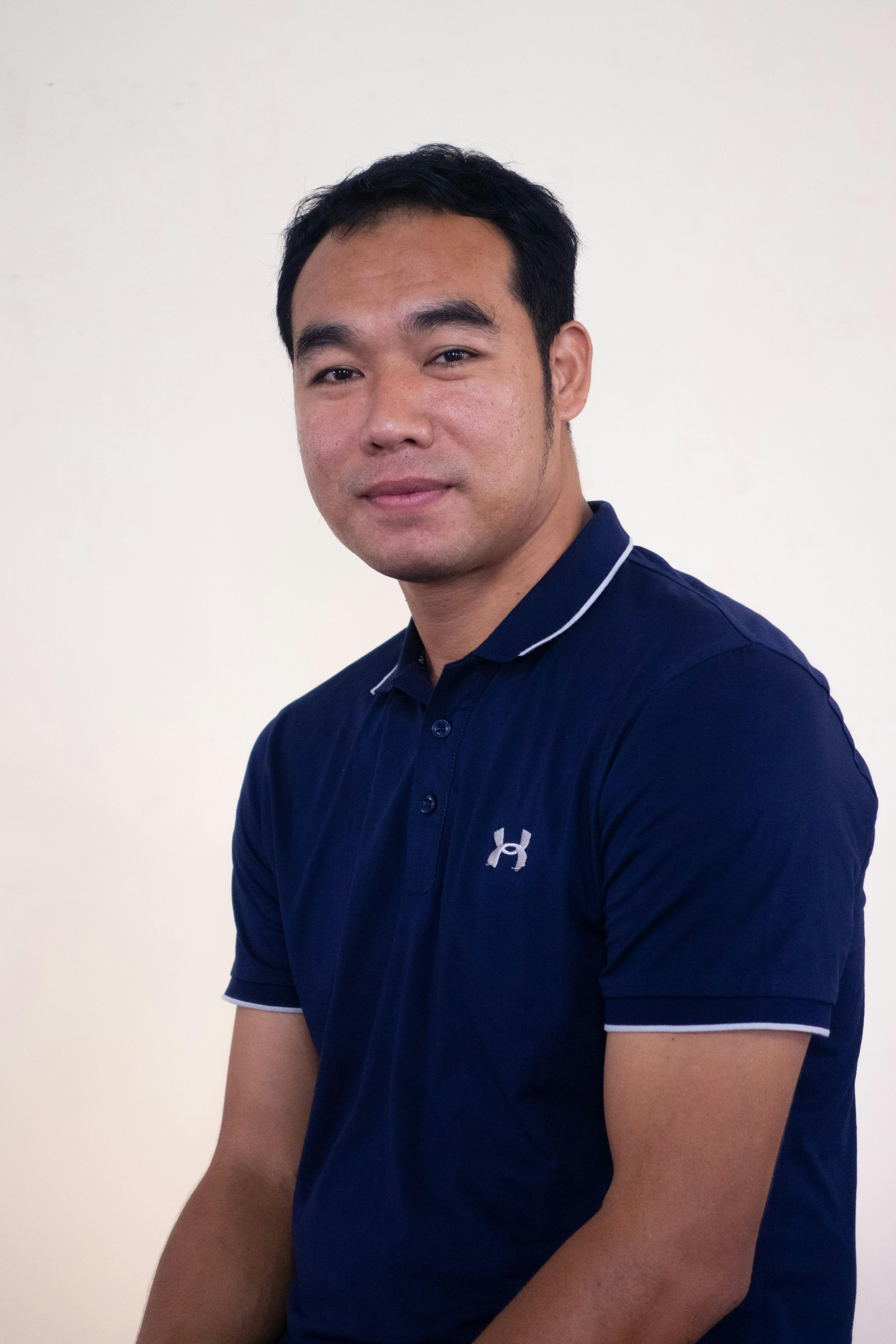 Studio portrait of an adult man in a blue polo shirt against a plain background.