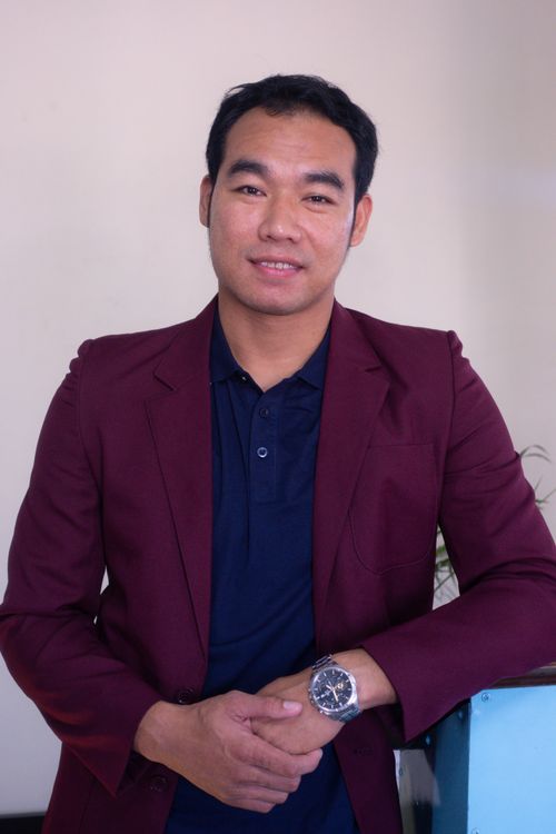 Free A confident adult man in a maroon jacket poses indoors with a smile, embodying professionalism and charisma. Stock Photo