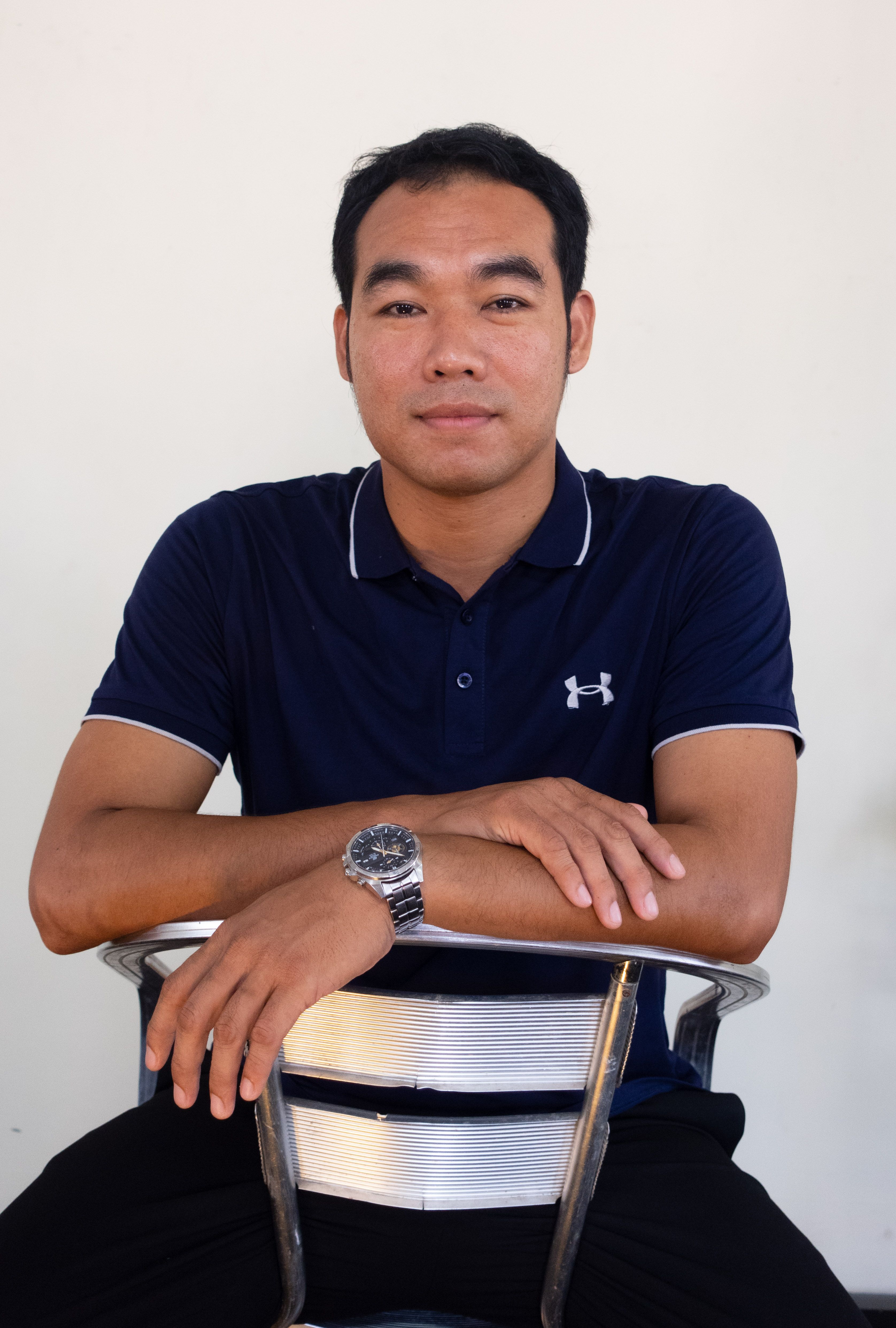 A man in a navy polo shirt casually sits on a metal chair.