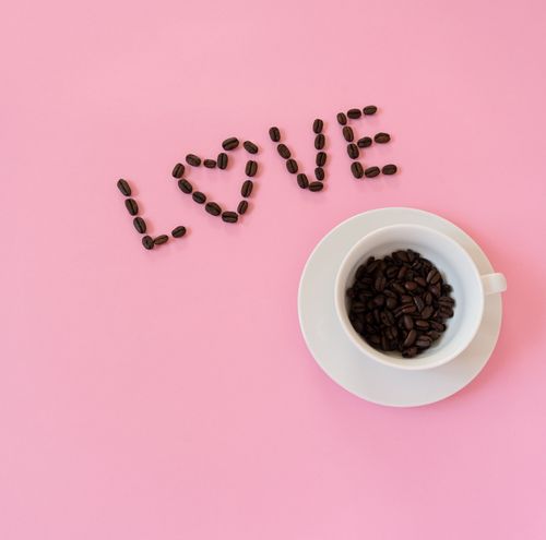 Free Coffee bean arrangement spelling 'LOVE' beside a cup on a pink background. Perfect for coffee lovers. Stock Photo
