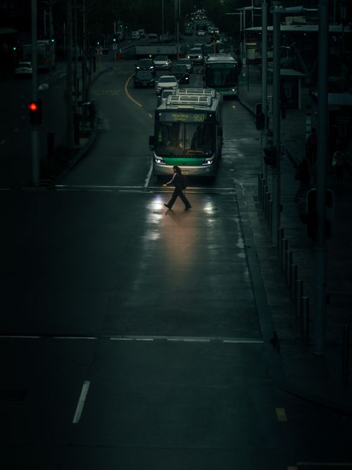 Free A pedestrian crosses a rainy street in Perth, Australia, with reflected city lights creating a dramatic scene. Stock Photo