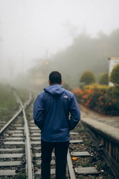 A solitary figure walks along railway tracks engulfed in fog, creating a mysterious scene.