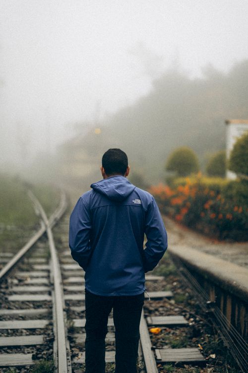 Free A solitary figure walks along railway tracks engulfed in fog, creating a mysterious scene. Stock Photo