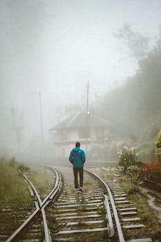 A solitary figure walks down mist-laden train tracks in a lush, foggy Sri Lankan landscape.