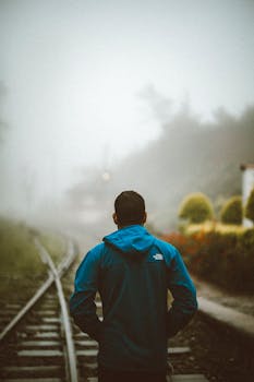 A man in a blue jacket stands on misty railway tracks in Sri Lanka, creating a mysterious ambiance.