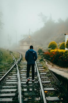 A lone man walks along mist-covered train tracks surrounded by lush greenery in Sri Lanka.
