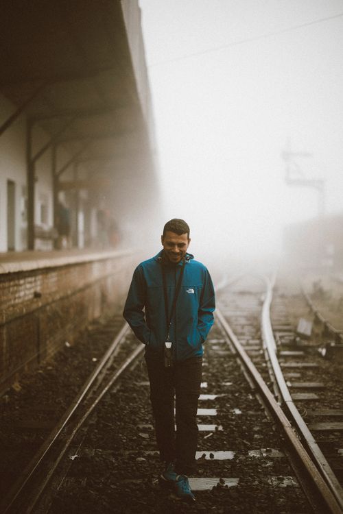 Free Man in blue jacket walking alone on foggy train tracks at a misty station. Stock Photo