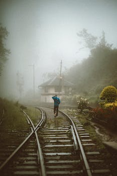 A lone traveler walks on a foggy railway track in Sri Lanka, surrounded by mist and greenery.